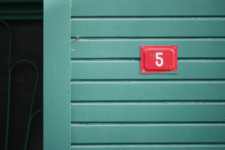 Door number five on a green wooden wall stands out clearlyの写真素材