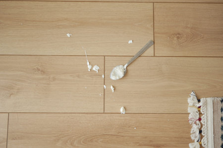 Spoon and spilled cream on wooden floor