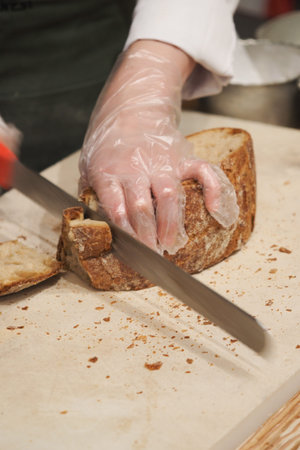 Hand cuts bread on a wooden board in a kitchen setting