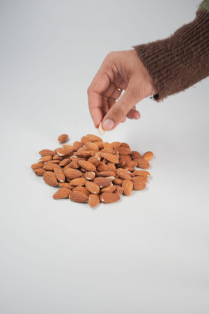 Hand picks almond from a pile on a white surfaceの写真素材