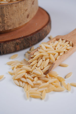 Orzo pasta spilled from wooden scoop on tableの写真素材