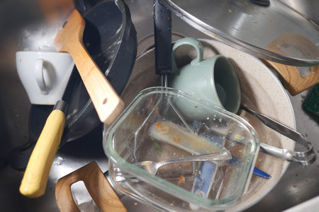 Dirty dishes and utensils piled in a kitchen sinkの写真素材