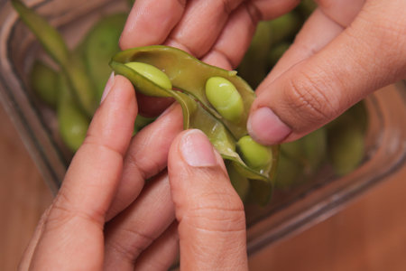 Hands shelling edamame beans in a glass bowl