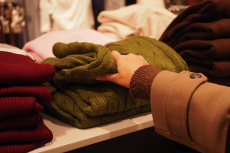Hand reaches for green sweater in clothing store