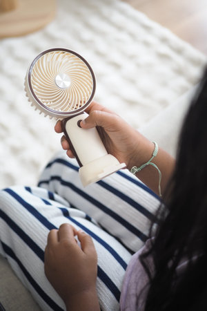 Child holds portable fan in living room on a warm day