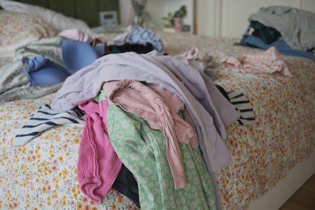 Clothes scattered on a bed in a bedroomの写真素材