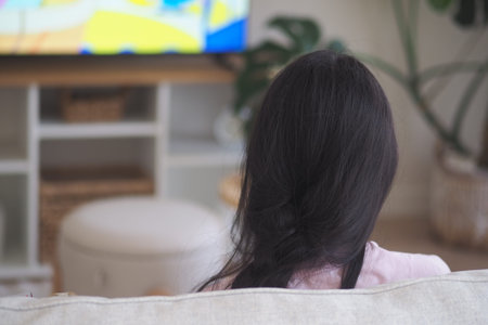 A child sits on a sofa looking at a television in a living roomの写真素材