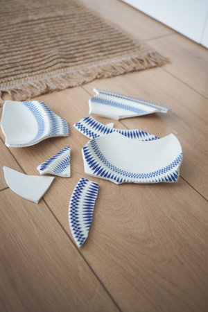 Broken pieces of a ceramic plate on wooden floorの写真素材