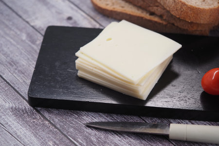 Cheese slices on a black board with bread and tomato