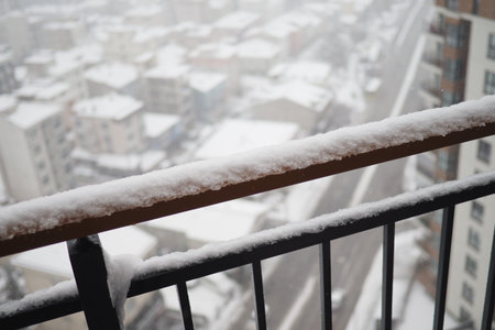 Snow covers balcony railing in a city during winterの写真素材