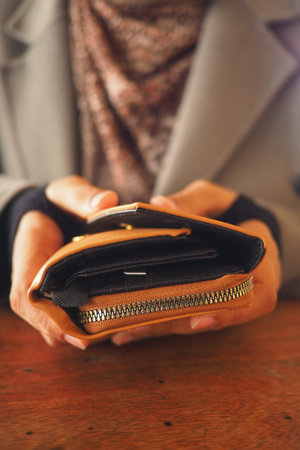 Person holds a brown wallet with coins on a wooden table