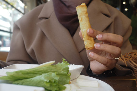 Person holding a spring roll near fresh vegetables in cafe