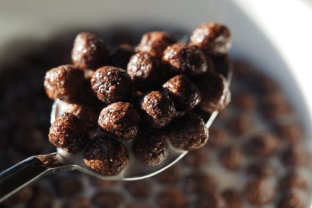 Brown cereal balls in milk on a spoon ready to eat