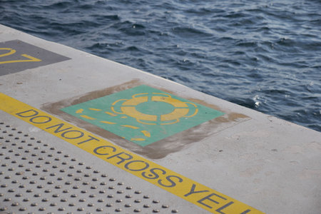 Warning sign on dock near ocean waves in bright sunlightの写真素材