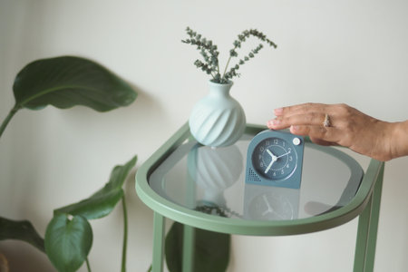 Hand placing clock on green table with plant and vase
