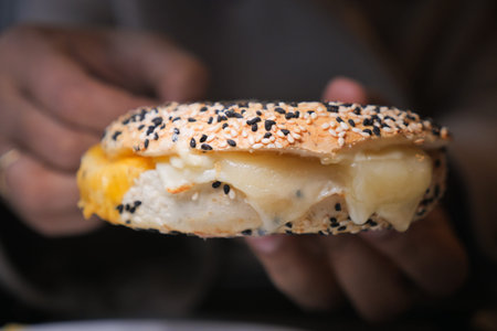 Bagel with cheese filling held by person in cafe setting