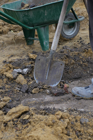 Worker digs soil near wheelbarrow on construction site