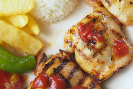 Grilled chicken with rice and fries served on a plate