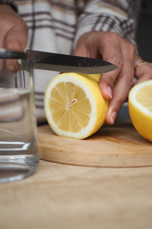 Cutting lemon on a wooden board near a glass of water