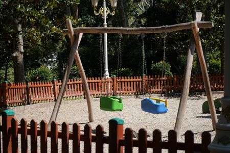 Swings in a playground near trees and a fence