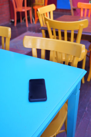 Colorful chairs surround a phone on a blue table. lost smart phone concept