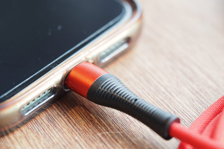 Phone connected to red audio cable on wooden table
