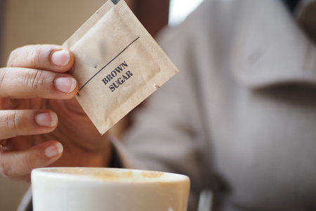 Expertly adding brown sugar to a warm drink in a cafeの写真素材