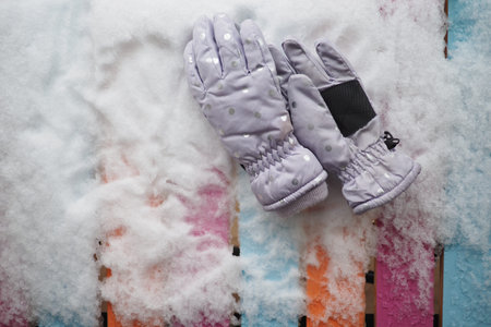 Warm gloves resting on colorful wooden surface in snowの写真素材