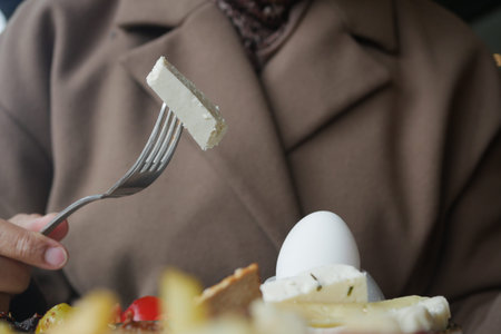 A person holds a fork with a piece of cheese. An egg is on the plate
