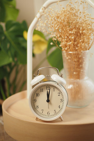 Clock on a wooden tray with dried flowers in a vase