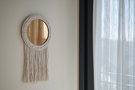 Woven mirror hangs on wall near window with curtains