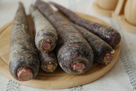 Purple carrots on a wooden plate in a kitchen settingの写真素材