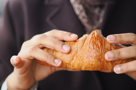 Hands hold a croissant in a cafe setting