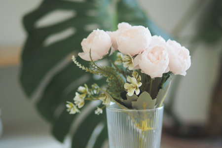 Flowers in a clear vase on a table with green leavesの写真素材