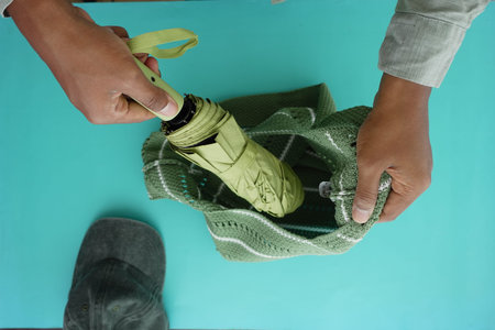 Hands prepare to place an umbrella into a bag on a tableの写真素材