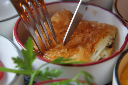 Eating turkish borek in a small dish with fork and knife