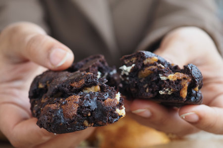 Hands hold broken chocolate cookies in a kitchen setting