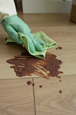 Cleaning a spill on wooden floor with a green cloth