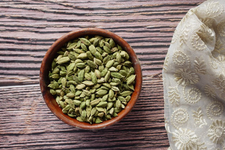 Bowl of green cardamom seeds on wooden table