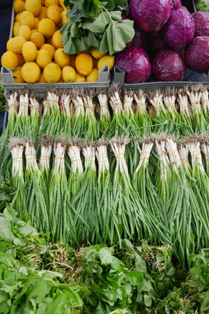 A market stall displays green onions, lettuce, lemons, and cabbage