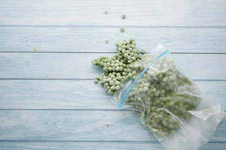 Frozen green peas spill on a wooden surface