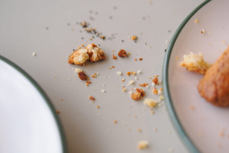 Crumbs scattered on a table near a plate with food pieces