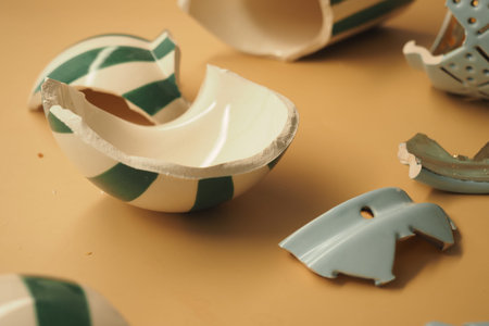 Broken ceramic pieces lie scattered on a flat surface with a green and white design