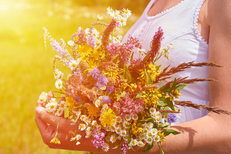A happy girl in white dress holding a bouquet of wildflowers in her hands on the green field. Nature and unity concept, herbs for alternative medicine.の写真素材