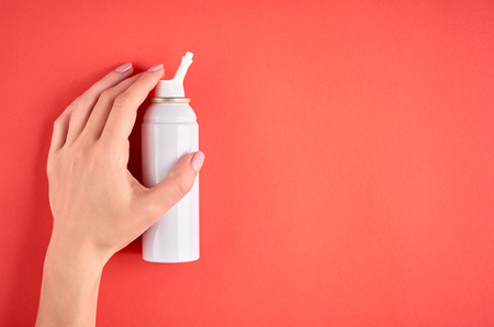 Nasal spray bottle composition with hand, white template bottle on pink background, flat lay and top view photoの写真素材