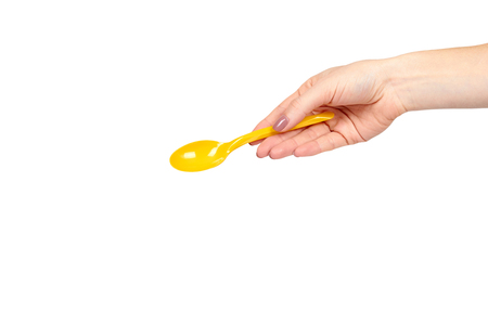 Hand with yellow plastic spoon, disposable utensil. Isolated on white background. Copy space templateの写真素材