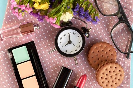 Alarm clock with flowers, mascara, cookies and pomade on blue background composition. Flat lay and top view photoの写真素材