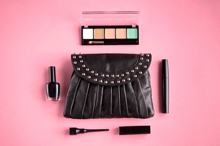 Black leather bag with nail polish, pomade, mascara and eye shadows on pink background composition. Flat lay and top view photoの写真素材