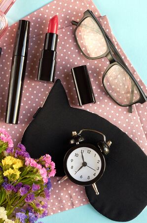 Sleep mask with alarm clock, flowers, mascara and pomade on blue background composition. Flat lay and top view photoの写真素材