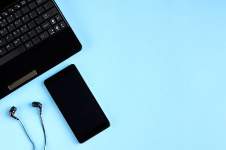 Black laptop keyboard, cellphone and headphones on blue background composition. Flat lay and top...